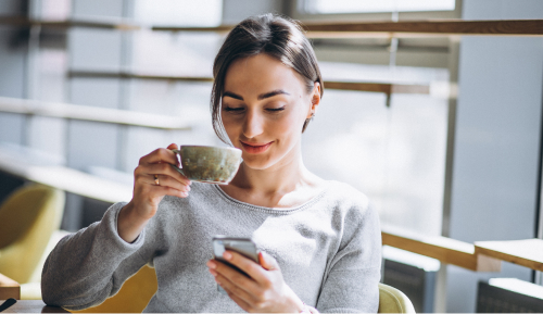 A woman drinks coffee and looks at her cell phone