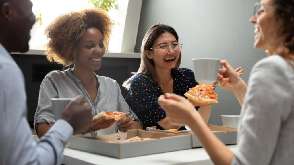 Employees sit around a table during lunchbreak and eat pizza together