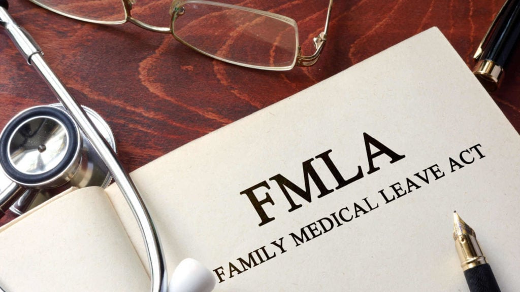A page with the words “FMLA family medical leave act” on a table with a stethoscope