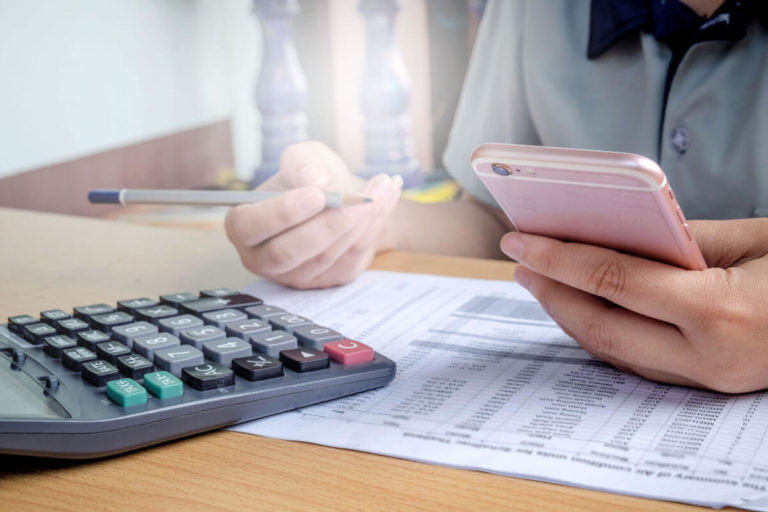 A payroll worker use pen and paper, a phone, and a calculator attempting to figure out how to calculate PTO.