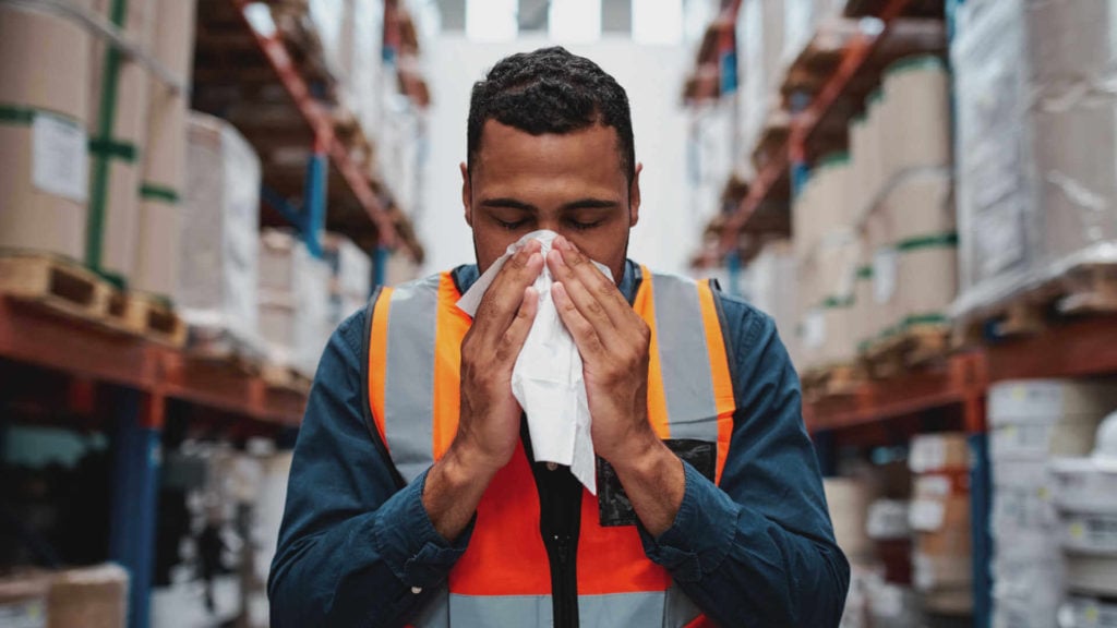 A sick worker blows his nose in the middle of a warehouse