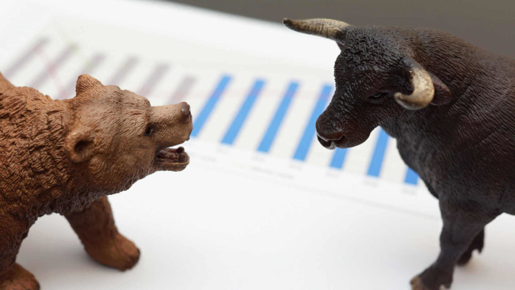 A toy bull and bear stand on a white paper showing a graph