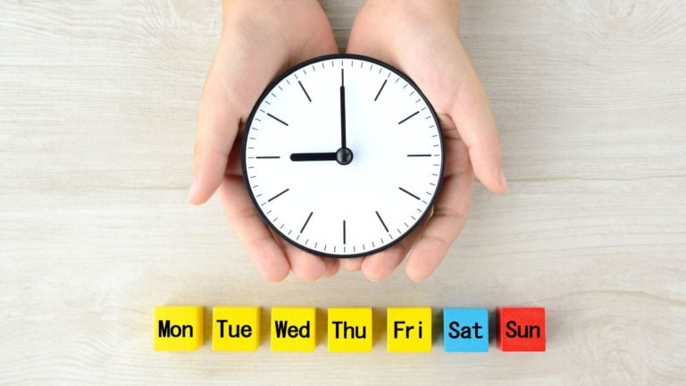 Clock covered by hands next to blocks showing the weekdays