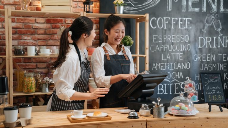 Two happy and engaged female restaurant workers stand behind the counter in a coffee shop