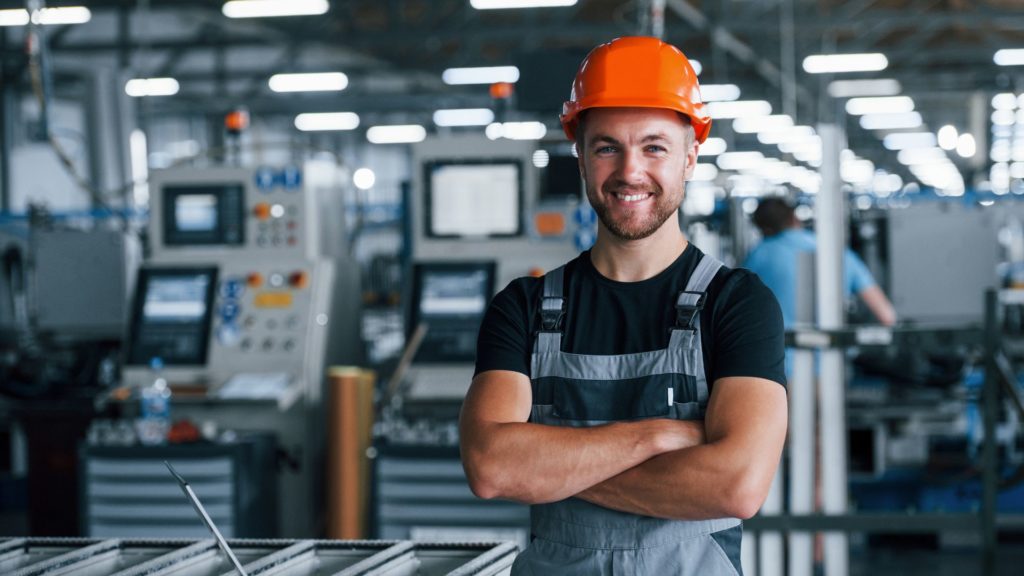 A happy and engaged factory worker smiles with machines in the background