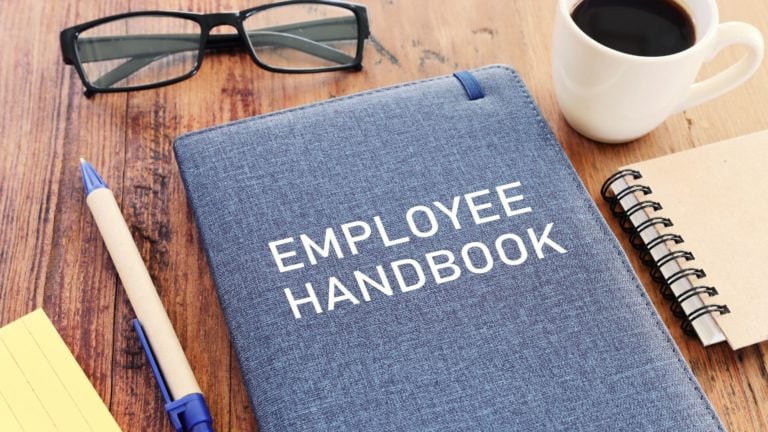 An employee handbook sits on a wooden office table