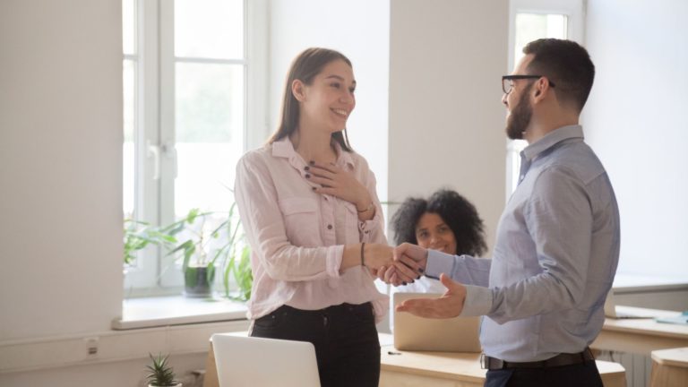 A male boss congratulates a female employee with a handshake