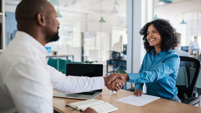 Smiling hr manager sitting at his desk in an office shaking hands with a job applicant