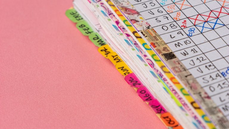 A folder full of task tracking papers lies on a pink background.