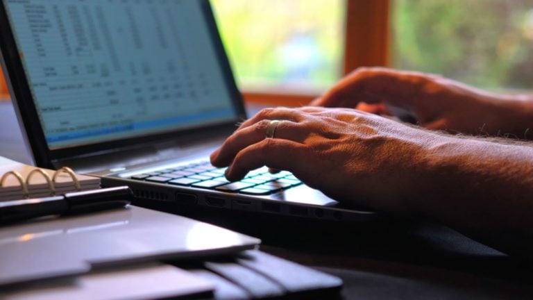 : A man enters data into a Google Sheets Timesheet on his laptop