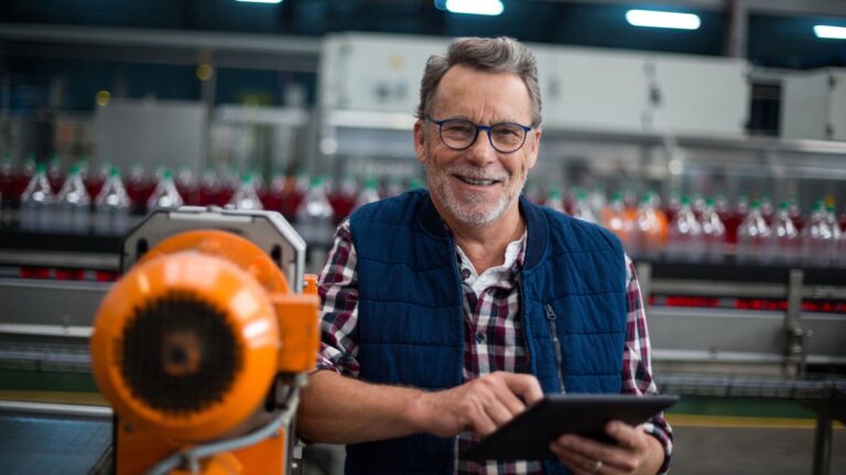 A smiling factory worker standing with a digital tablet in a factory