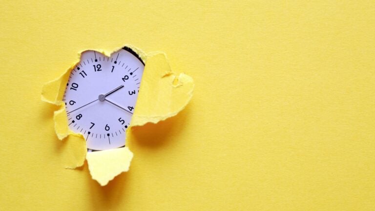 An analog clock can be seen through the hole in a yellow piece of paper.