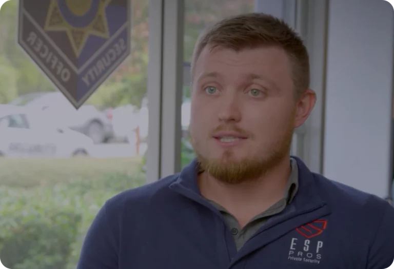 An ESP Pros Private Security team member speaking on camera, with a security officer badge visible on the window behind him