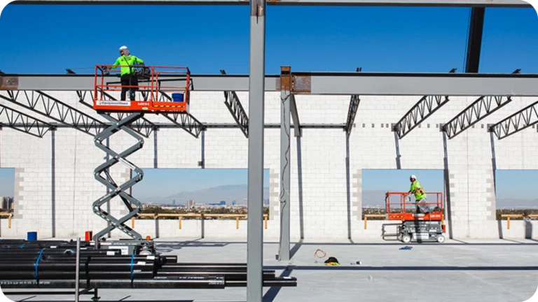 Construction workers on scissor lifts inside steel building frame